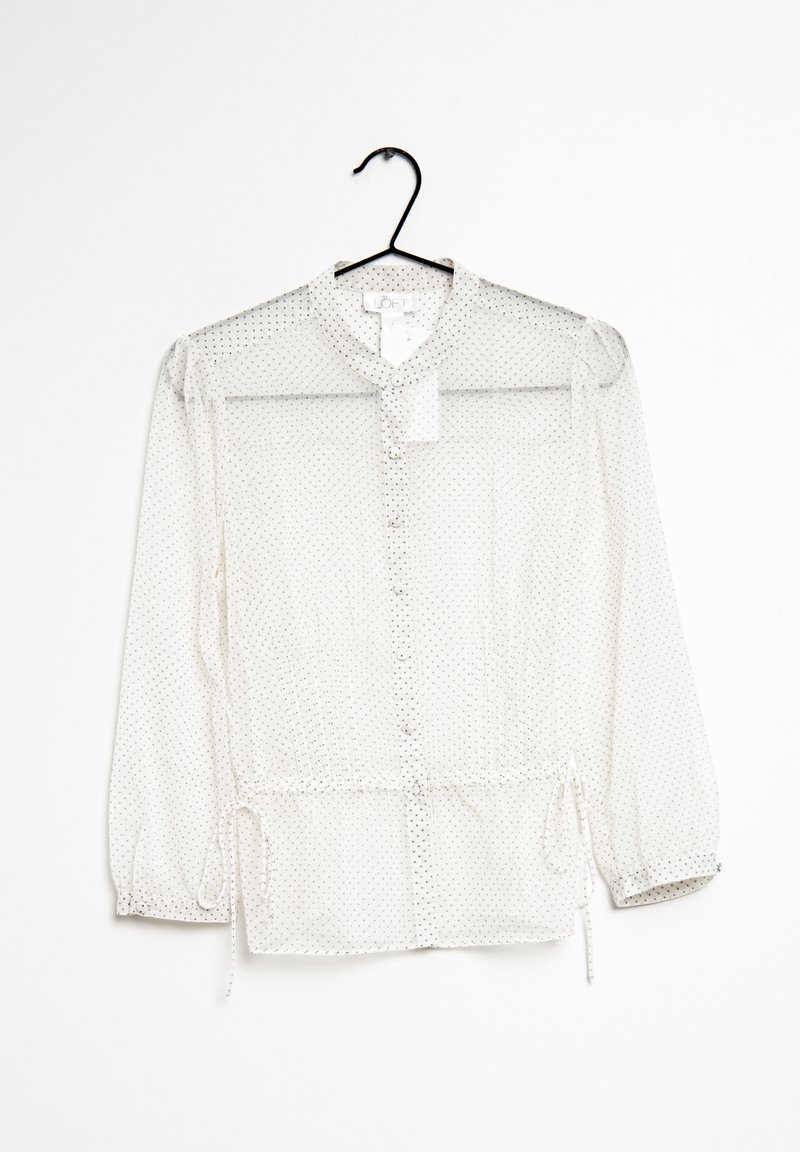 Blusa blanca transparente con cuello redondo, cierre de botones y dobladillo ajustable con cordón. Presenta pequeños lunares negros y mangas largas.