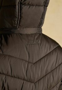 Tmavo hnedá nafukovacia bunda so šikmým prešívaním, s vyšívaným logom "JOULES" na zadnej strane, hladká textúra a kapucňa.