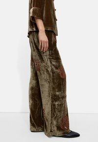 Sukienka z weluru w oliwkowej zieleni ze wzorami kwiatowymi w kolorze bordo, z szerokimi spodniami i bluzką z krótkim rękawem. Czarne szpilki.