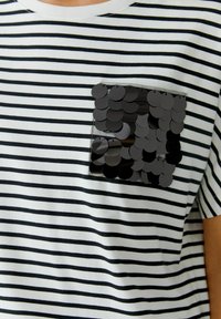 Schwarz-weiße gestreifte T-Shirt mit einer strukturierten schwarzen Pailletten-Tasche. Runder Ausschnitt und kurze Ärmeln. Aus Baumwollmaterial.