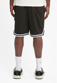 Svart idrettsshorts med hvit kant, laget av mesh-stoff. Båret med hvite ankelsokker og svarte/hvite joggesko.
