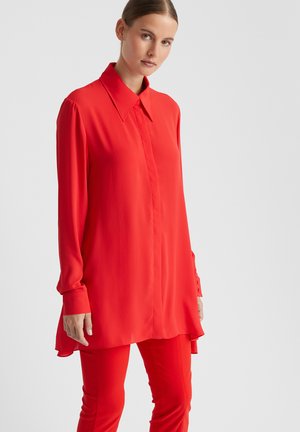 Rode blouse met lange mouwen en puntige kraag, zachte textuur, asymmetrische rand en met knopen afgesloten manchetten, gecombineerd met bijpassende slim-fit broek.