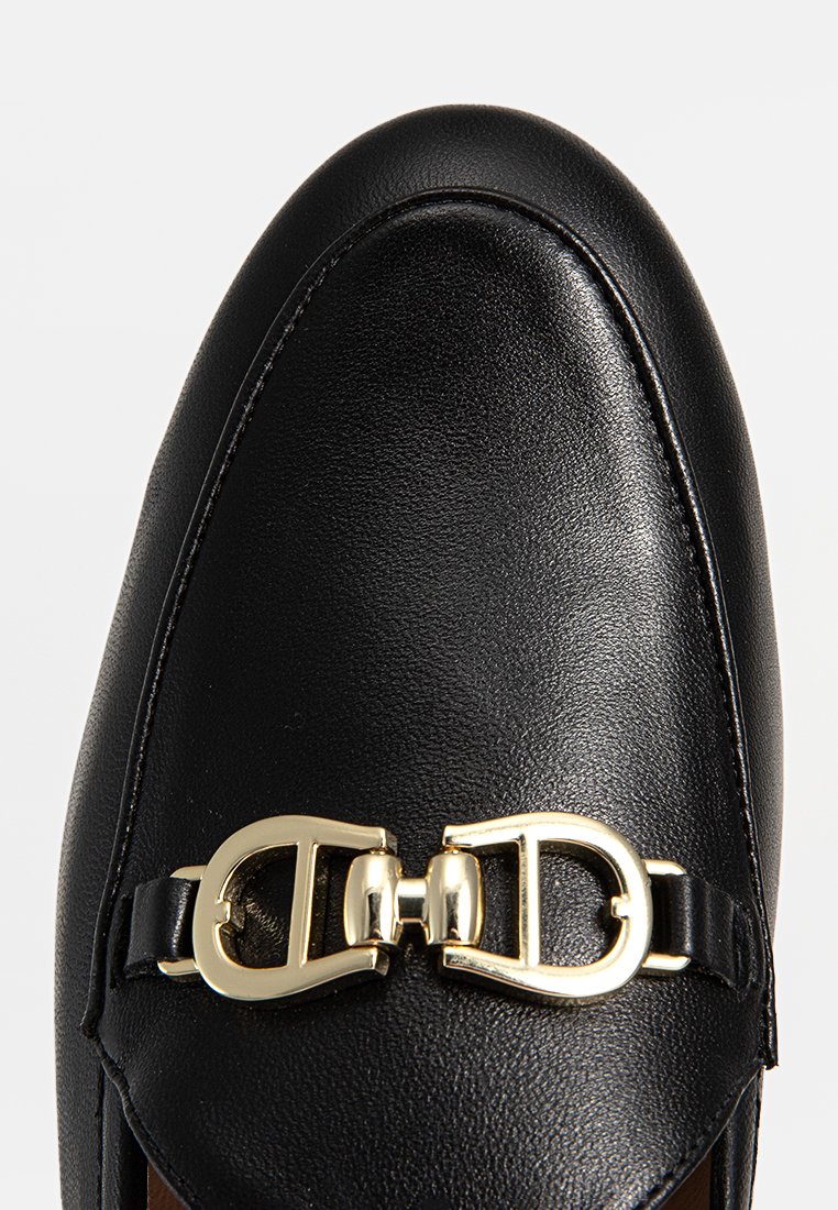 Mocassin en cuir noir avec un bout arrondi et un accent en boucle dorée. Texture lisse et design simple sans embellissements supplémentaires.