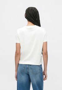 Hvit t-skjorte med korte ermer og rund hals, laget av mykt stoff, med avslappet passform og subtile sømdetaljer. Kombinert med blå jeans.