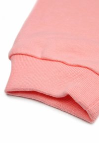 Lichtroze katoenstof met geribbelde manchet details. Zachte textuur en een gladde afwerking, netjes gevouwen om de vorm en de naad te tonen.