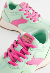Miętowo-zielone sneakersy z różowymi akcentami i sznurowadłami. Posiadają gładki materiał, wyściełane wnętrze oraz złote logo na języku.