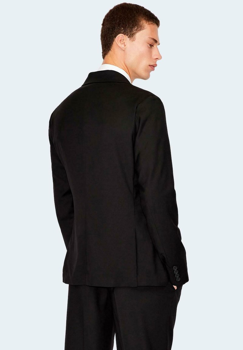 Chaqueta de traje negra con un corte ajustado, solapas muesca y cierre de un botón, fabricada en tela suave con detalles de costura sutiles.