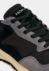 Baskets combinant du daim noir et gris avec des matériaux textiles, dotées d'une languette rembourrée, de lacets texturés et d'une semelle beige.