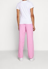 Hvid t-shirt med korte ærmer kombineret med lyserøde, løstsiddende bukser. Sættet afsluttes med hvide sneakers.
