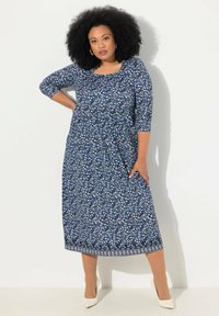 Sukienka o średniej długości w ciemnoniebieskim materiale z białym i jasnoniebieskim wzorem kwiatowym. Kwadratowy dekolt, rękawy 3/4 oraz warstwowy krój u dołu.