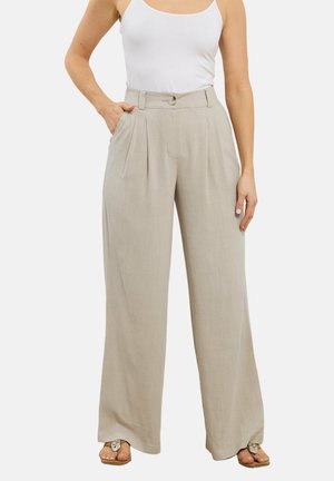 Kvinde iført lyse beige bukser med høj talje og vide ben med folder, en hvid ærmeløs top og flade sandaler.