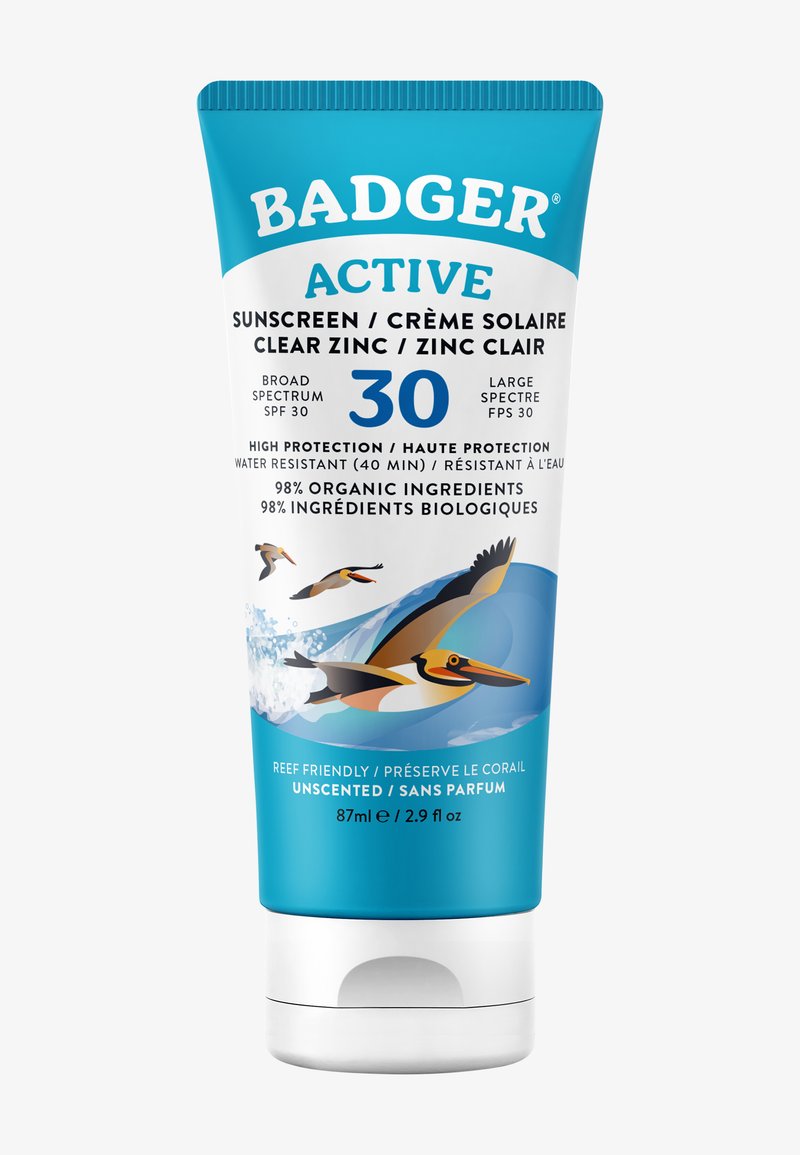 Tubo di crema solare con un tappo blu e corpo bianco, caratterizzato da un design di uccelli e onde. Il testo include SPF 30, ingredienti biologici e informazioni sulla resistenza all'acqua.
