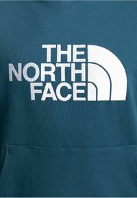 Tyrkysová mikina s kapucí, vybavená kapsou vpředu, vyrobená z bavlněné směsi, s výrazným bílým logem "THE NORTH FACE".