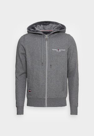 Sweat à capuche gris zippé avec cordons, poches avant, logo « Tommy Hilfiger EST. 1985 » sur la poitrine et petite étiquette drapeau près de la poche.