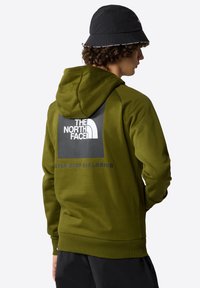 Felpa verde oliva con logo sul retro che presenta un quadrato nero e testo bianco. Il testo recita "THE NORTH FACE" e "NEVER STOP EXPLORING."
