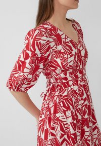 Rood en wit gestreepte jurk met een V-hals, pofmouwen en een getailleerde taille. Heeft abstracte bladeren en vormontwerpen.