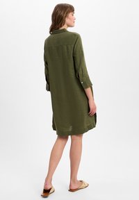 Olivegrünes Leinenkleid mit Kragen, aufrollbaren Ärmeln, Rückenschlitzdetails und seitlichen Schlitzen; knielang mit einer lockeren Silhouette.