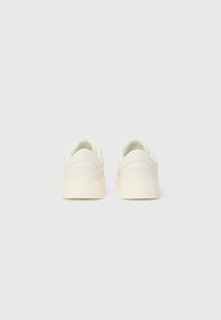 Cream-colored sneakers with a smooth leather upper, rounded shape, cushioned collar, and textured rubber sole featuring a logo detail.