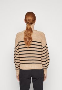 Suéter de punto beige con rayas horizontales negras, que presenta un dobladillo acanalado y mangas abullonadas. La parte trasera muestra un ajuste holgado.