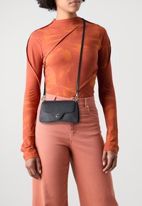 Borsa a tracolla nera in pelle con finitura testurizzata, patta curva e un accento dorato, abbinata a un top arancione aderente a maniche lunghe e pantaloni rosa.