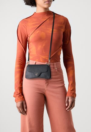 Borsa a tracolla nera in pelle con finitura testurizzata, patta curva e un accento dorato, abbinata a un top arancione aderente a maniche lunghe e pantaloni rosa.