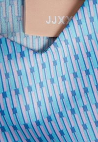 Textil med geometriskt mönster i nyanser av blått och rosa; har en etikett med präglad text "JJXY" i en kontrasterande ljus färg.