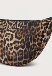 Pussäväs leopardikuosisesta kankaasta; puolipyöreä muoto, jossa vetoketjukiinnitys; mustia ja ruskeita pilkkuja; brändätty "HUGO" -logolla.