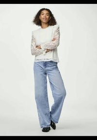 Top branco de renda com mangas bufantes, combinado com jeans amplos azuis claros e calçado preto. O conjunto apresenta detalhes delicados em renda.