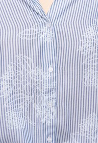 Μπλε και λευκό πουκάμισο με κάθετες ρίγες και λευκό λουλουδάτο σχέδιο, με κουμπιά στο μπροστινό μέρος και γιακά ορατό στο πάνω κέντρο.