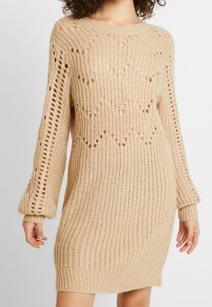 Beige gebreid jurk met een losse pasvorm, textuur ribbelingen en open weefpatroon. Lange mouwen met aansluitende manchetten en ronde halslijn.