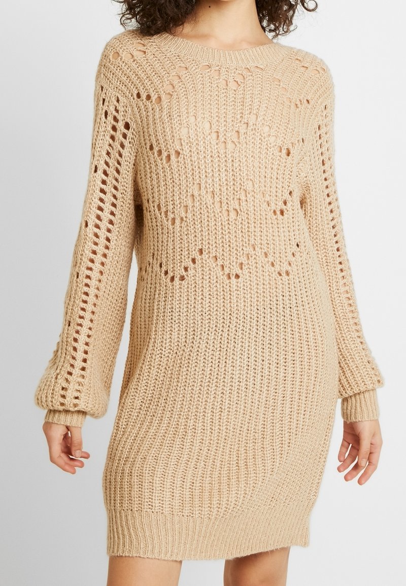 Abito maglione beige in maglia, caratterizzato da una vestibilità ampia, righe testurizzate e un motivo a trama aperta. Maniche lunghe con polsini aderenti e scollatura rotonda.