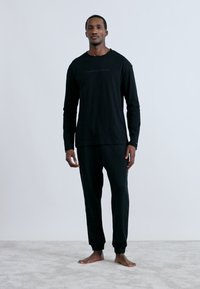 Czarna koszula z długim rękawem oraz dopasowane spodnie wykonane z miękkiego materiału, z prostym wzorem i małym logo na przedniej części koszuli.
