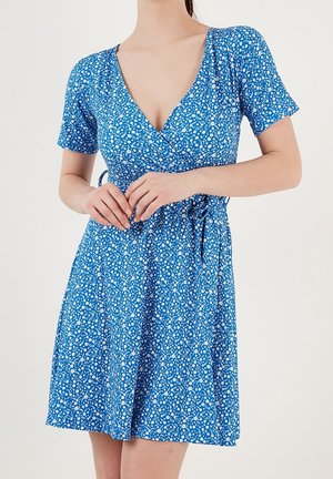 Niebieska kwiecista sukienka kopertowa z krótkimi rękawami, dekoltem w kształcie litery V i wiązaniem w talii. Wzór z małych białych i zielonych kwiatków na całej powierzchni. Gładki materiał.