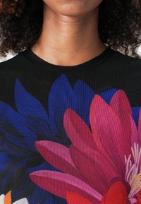 Zwart T-shirt met een levendig bloemenontwerp met grote roze en blauwe bloemblaadjes. Zachte textuur, ronde hals en korte mouwen.