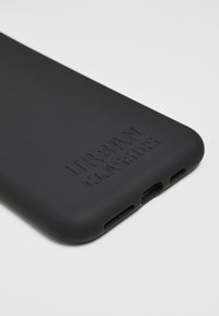 Huse de telefon din silicon negru cu logo embosat "URBAN CLASSICS", cu decupaje pentru porturile de încărcare și audio, textură netedă.