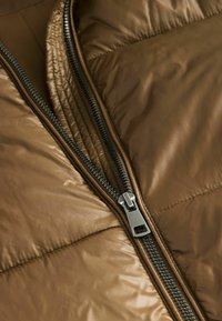 Brun pufferjakke med synlig lynlås og kviltet tekstur. Stoffet ser glat ud med en let glans. Lynlåsen har sølvfarvet hardware.