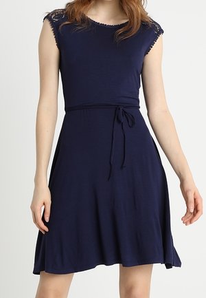 Granatowa sukienka bez rękawów sięgająca kolan, z koronkową lamówką na ramionach i cienkim paskiem wiązanym w talii.