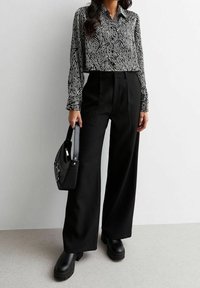 Camicia a maniche lunghe a motivi bianco e nero, pantaloni neri a vita alta, borsa nera e stivali neri massicci. Tessuto liscio, vestibilità ampia.