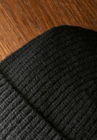 Zwarte gebreide muts met ribbelpatroon, gemaakt van dikke garen, met een zachte, harige afwerking en een ronde bovenkant.