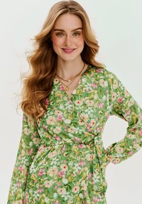 Zelené kvetinové zavinovacie šaty s dlhými rukávmi, s kombináciou ružových, bielych a žltých kvetov, textúrovanou tkaninou a detailom viazania v páse.