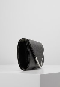 Musta pieni laukku, jossa on teksturoidun pinnan viimeistely ja hopeinen yksityiskohta. Suunnittelu on kompakti ja suorakulmainen, ja siinä on läppäkiinnitys.