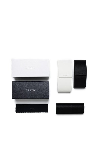 Accessori Prada: due custodie in pelle nera, una custodia in pelle bianca e due scatole nere e bianche, con superfici testurizzate e marchiatura.