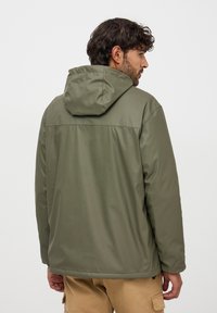 Giacca impermeabile verde oliva con cappuccio, caratterizzata da una texture liscia, polsini elasticizzati e un design semplice. Dettagli delle cuciture si estendono sul retro.