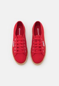 Red canvas sneakers with a textured jute sole, featuring six eyelets and matching laces. Brand logo on the tongue and side.