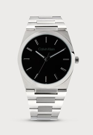 Ανδρικό ρολόι Calvin Klein με μαύρο στρογγυλό καντράν, ασημένιους δείκτες ωρών και ασημένιο μεταλλικό μπρασελέ.