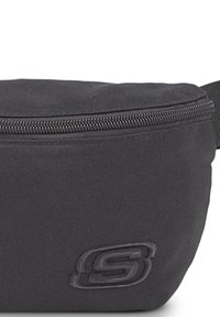 Riñonera de tela negra con forma redonda, superficie texturizada, cierre con cremallera superior y un logotipo grabado prominente en la parte frontal.