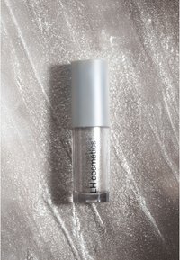 Brillo labial de purpurina plateada en un tubo transparente con tapa plateada mate, que presenta una textura suave y un brillo reflectante sobre un fondo claro.