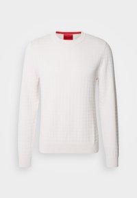 Pull en tricot blanc à manches longues avec un motif en grille subtil et un col rond, avec une étiquette de marque rouge à l'intérieur du col.