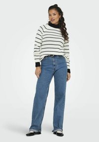 Knit sweater in cream with black stripes, paired with high-waisted blue jeans. Sweater has ribbed cuffs, jeans are wide-leg with frayed hem.