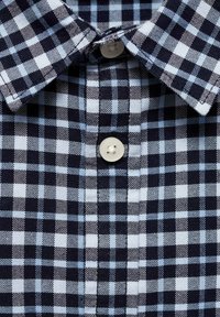 Chemise à carreaux bleu marine et bleu clair avec un col boutonné et une seule fermeture à bouton, fabriquée en tissu tissé à finition texturée.